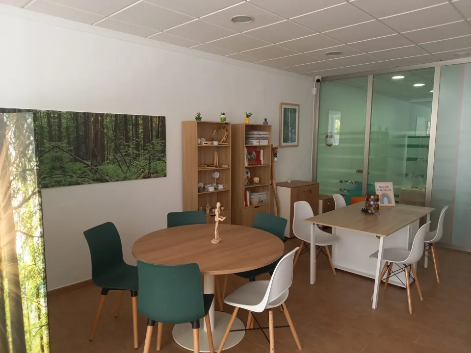 Sala de terapia grupal y arteterapia con mesas, sillas y un mural de bosque